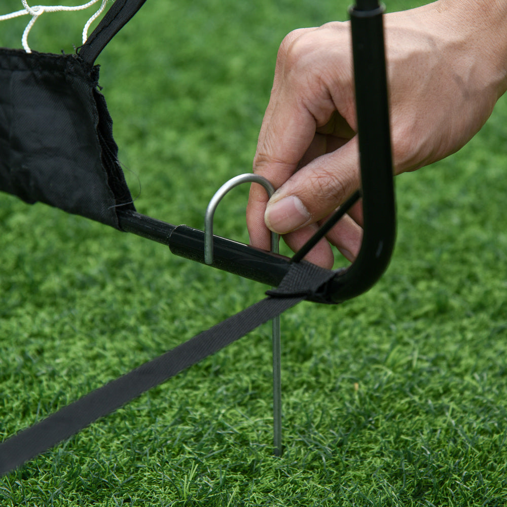 Nahaufnahme einer Hand, die einen Metallhering zur Stabilisierung des Tores in den Rasen drückt.