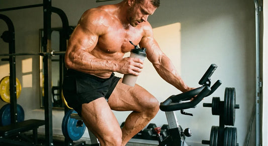 Muskulöser Sportler auf einem Heimtrainer mit einem Protein-Shake; Fokus auf Muskelaufbau und Cardio.