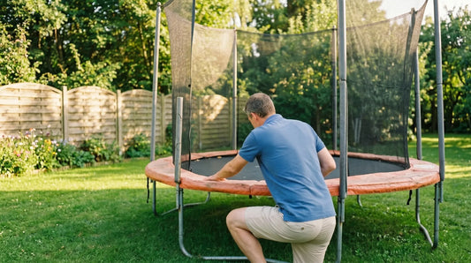 Familienvater inspiziert Trampolin-Sprungtuch im sonnigen Garten — Vorbereitung für den Sprungtuch-Wechsel.