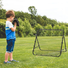 Ein kleiner Junge übt mit dem Rebounder auf einer grünen Wiese seine Ballkontrolle.