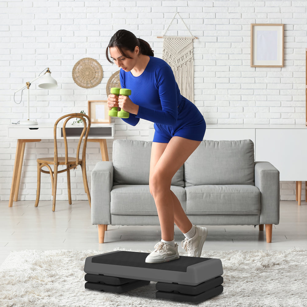 Frau beim Hanteltraining auf dem grauen Fitness Stepper im Wohnzimmer