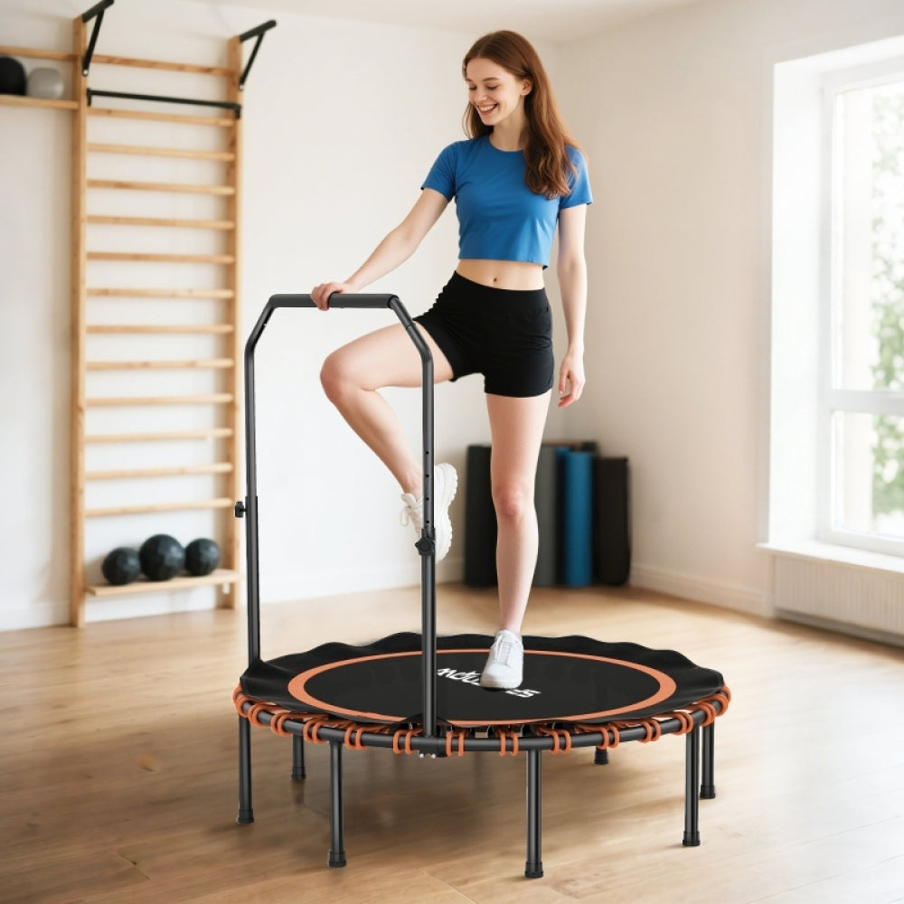 Frau in Sportkleidung steht einbeinig auf dem Trampolin, hält sich am Griff fest; Fokus auf die orangen Details.