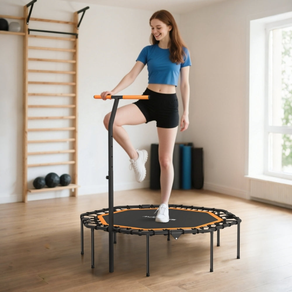 Frau in Sportkleidung trainiert auf dem Trampolin im Wohnzimmer, hält sich am Griff fest.