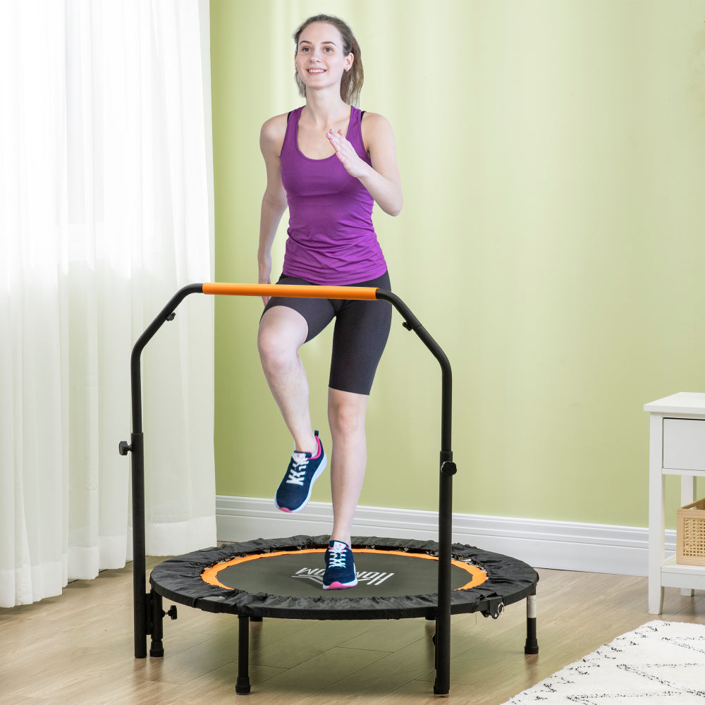 Frau in Sportkleidung trainiert auf dem Trampolin im Wohnzimmer, hält sich am orangen Griff fest.