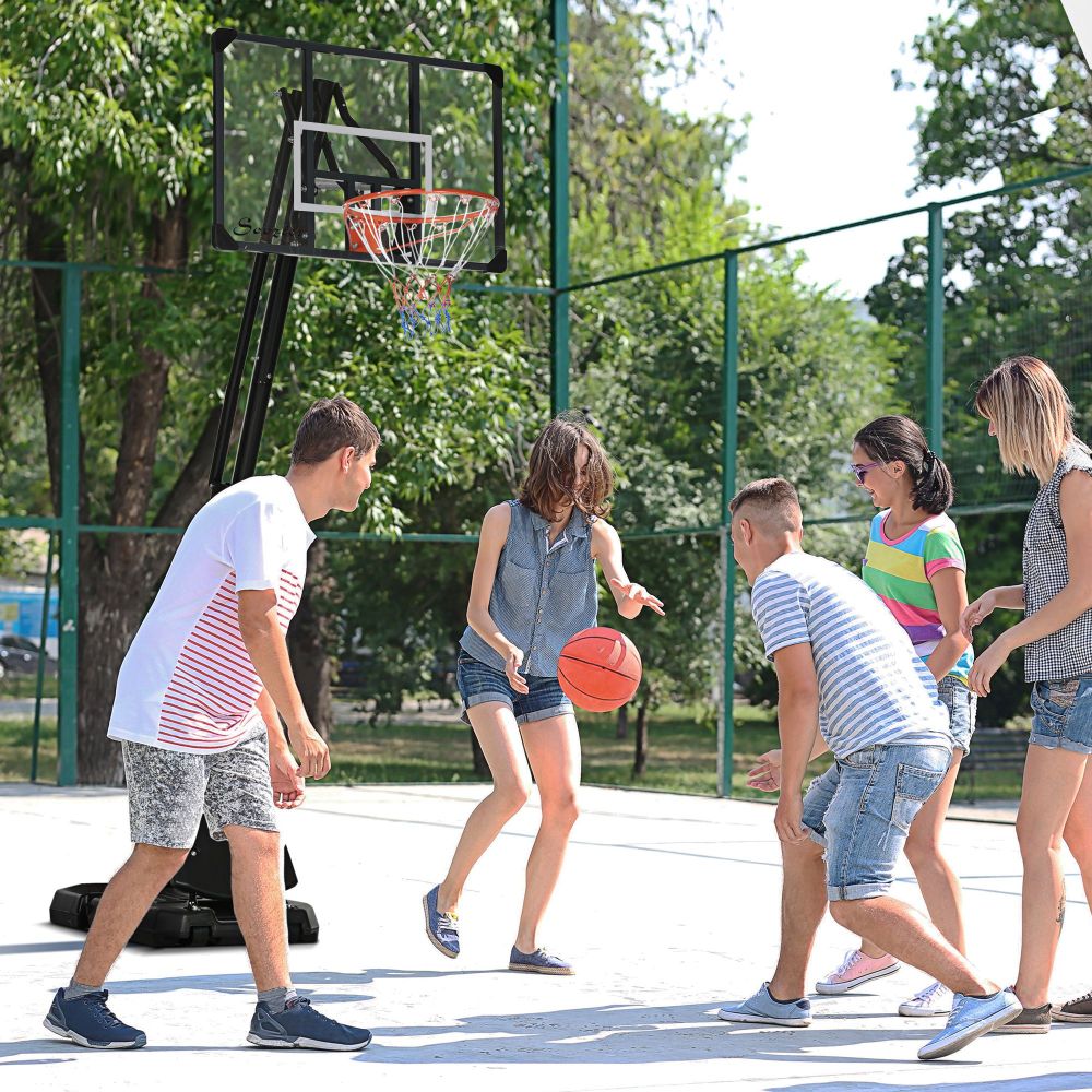 Gruppe von Jugendlichen spielt Basketball auf einem Sportplatz mit dem aufgebauten Ständer.