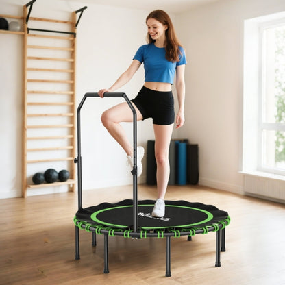Junge Frau trainiert einbeinig auf dem Trampolin, hält sich am Griff fest; Fokus auf die grünen Details.