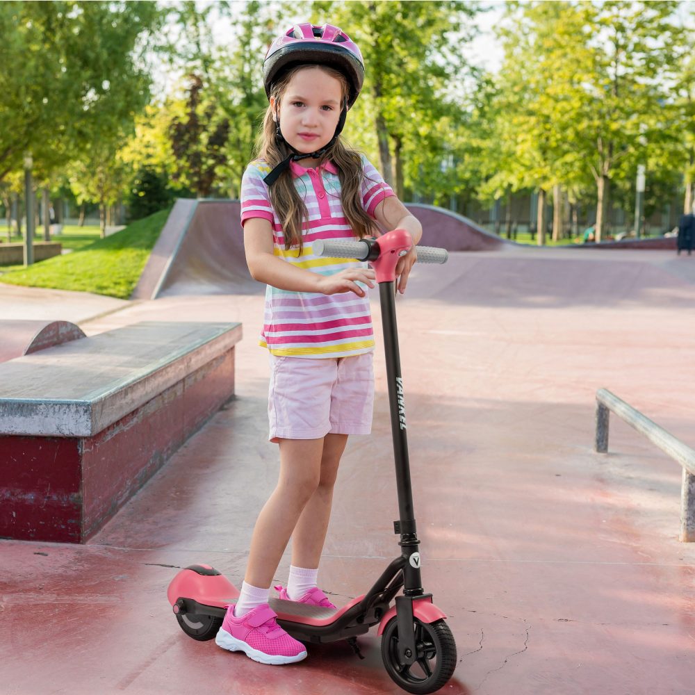 Mädchen fährt glücklich mit dem rosa E-Scooter und Schutzausrüstung im Park.
