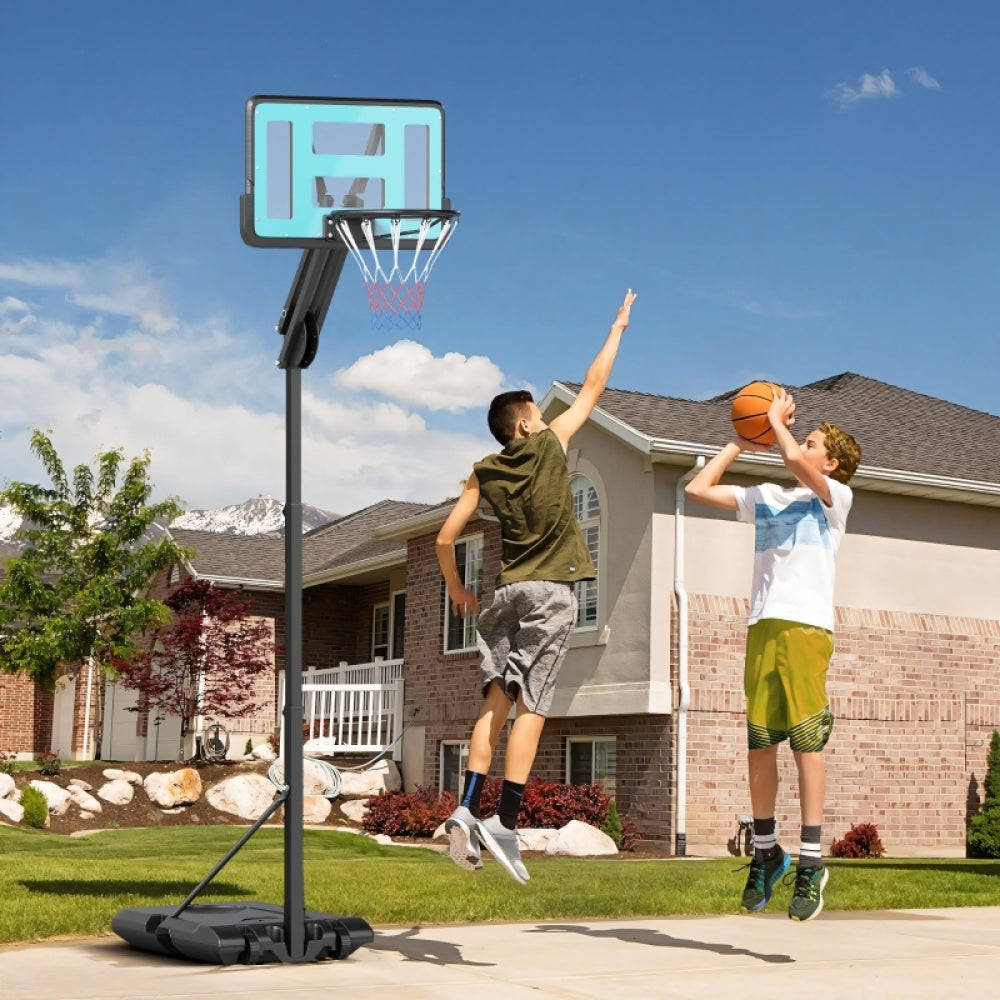 Zwei Kinder werfen Körbe auf den Basketballständer in einer Einfahrt vor einem Haus.